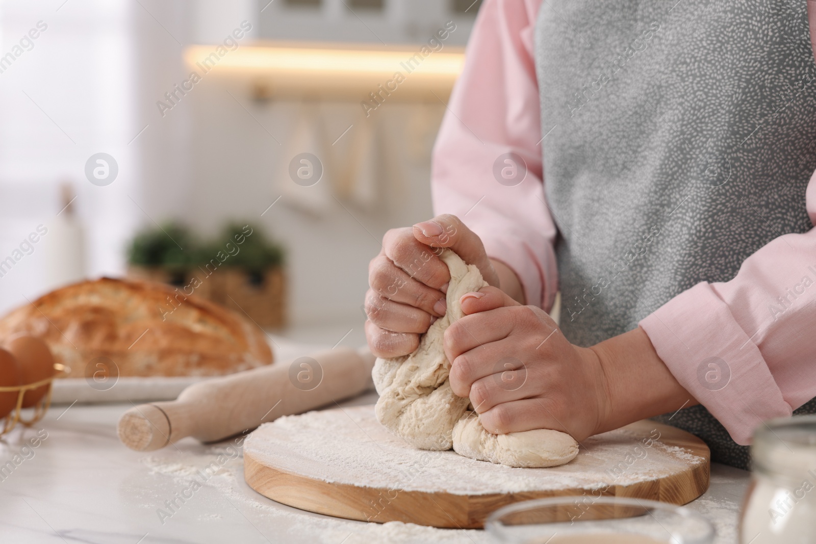 Photo of Making bread. Woman kneading dough at white table in kitchen, closeup