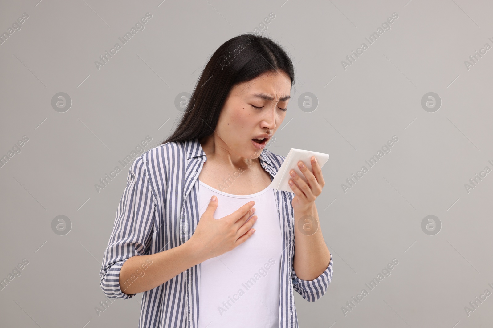 Photo of Suffering from allergy. Young woman with tissue sneezing on grey background