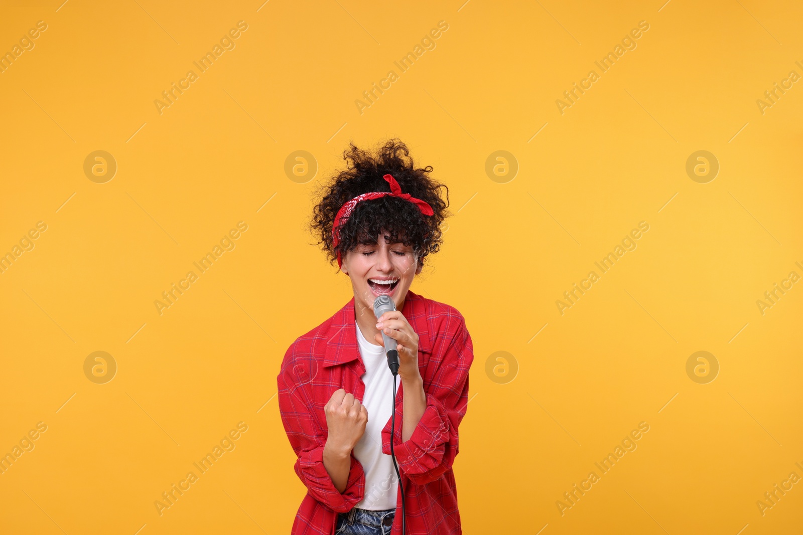 Photo of Beautiful young woman with microphone singing on yellow background