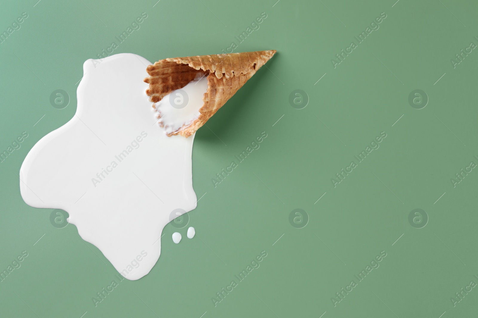 Photo of Melted ice cream and wafer cone on green background, top view. Space for text