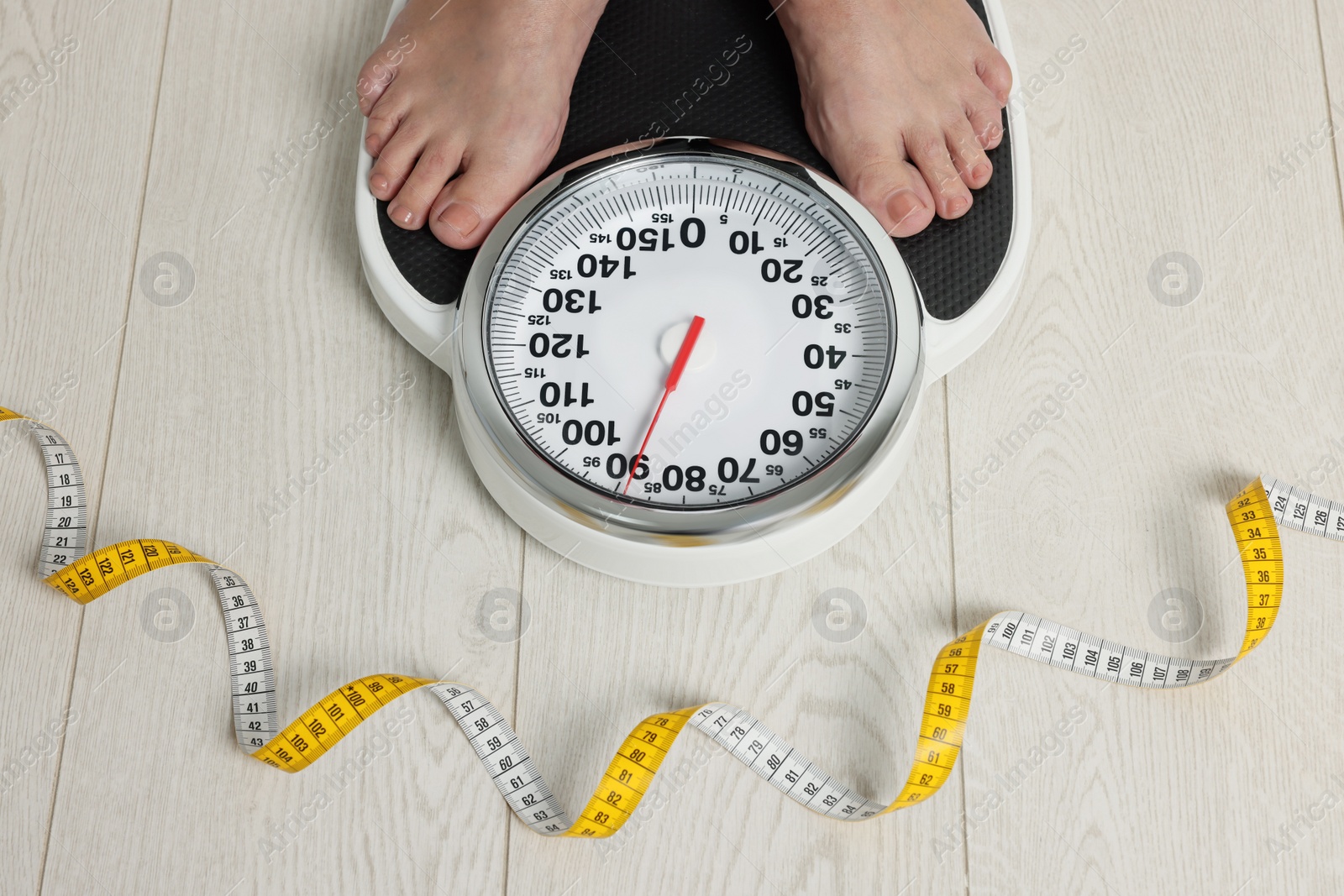 Photo of Closeup of woman using scales on floor near measuring tape, above view. Overweight problem