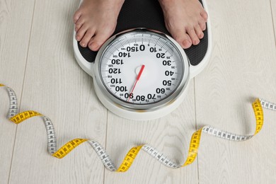 Photo of Closeup of woman using scales on floor near measuring tape, above view. Overweight problem