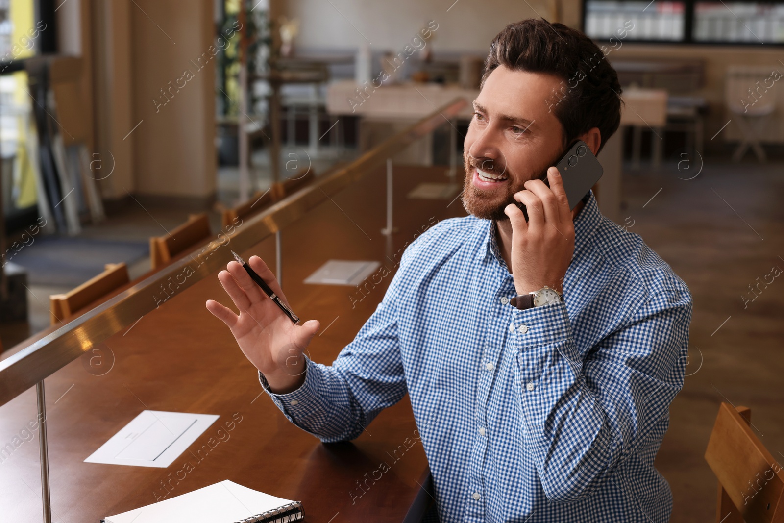 Photo of Handsome man talking on phone at table in cafe