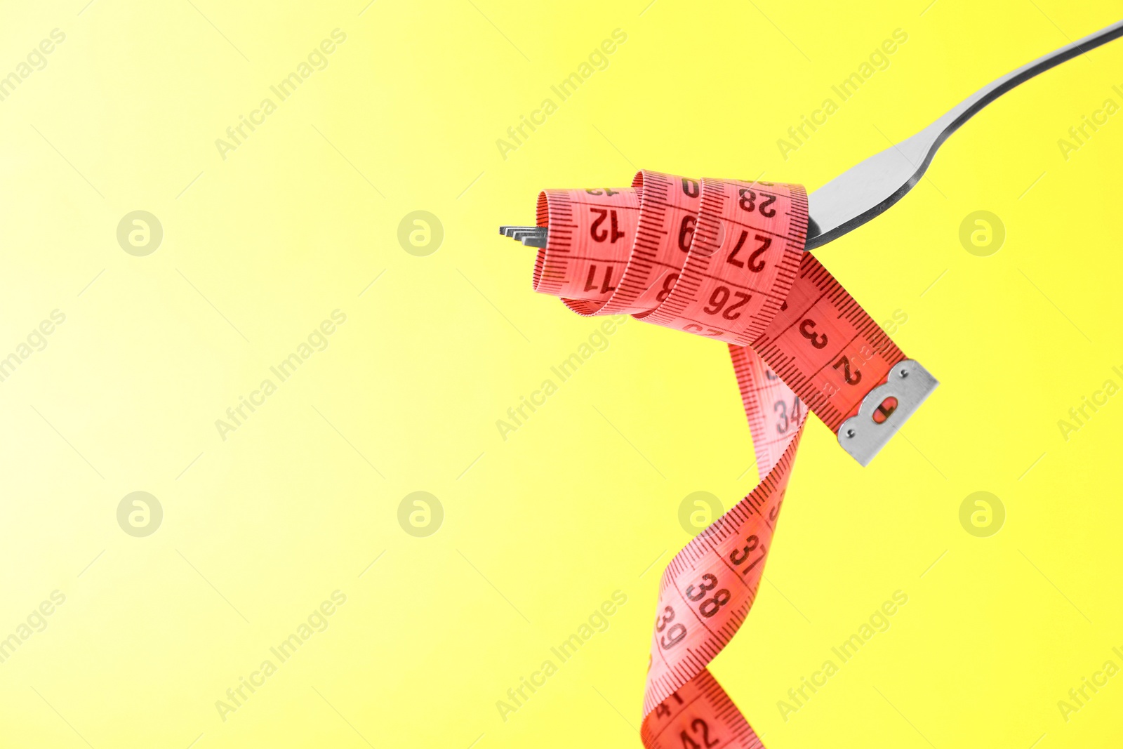 Photo of Fork with measuring tape on yellow background, space for text. Diet concept