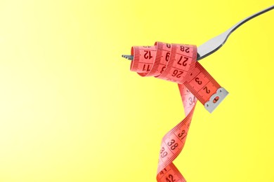 Photo of Fork with measuring tape on yellow background, space for text. Diet concept