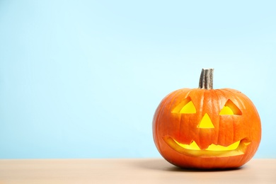 Photo of Scary jack o'lantern pumpkin on light blue background, space for text. Halloween decor