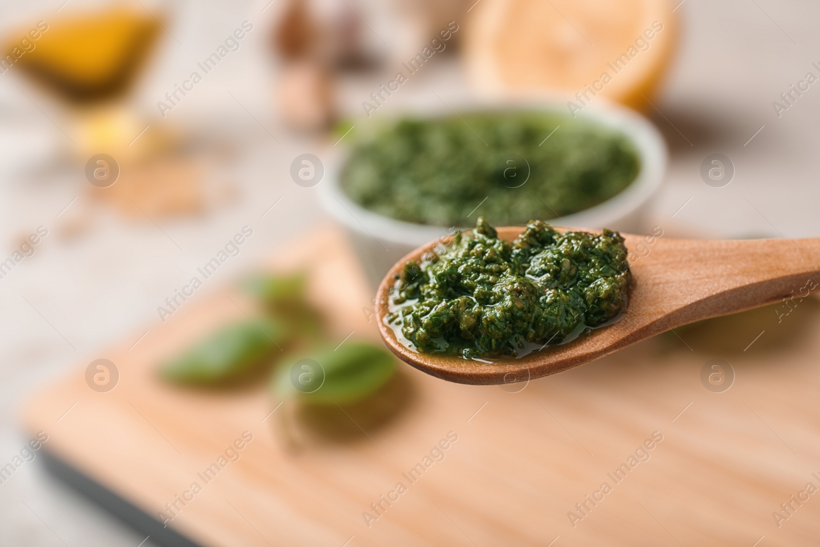 Photo of Homemade basil pesto sauce in wooden spoon over table, closeup