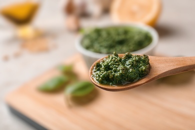 Photo of Homemade basil pesto sauce in wooden spoon over table, closeup