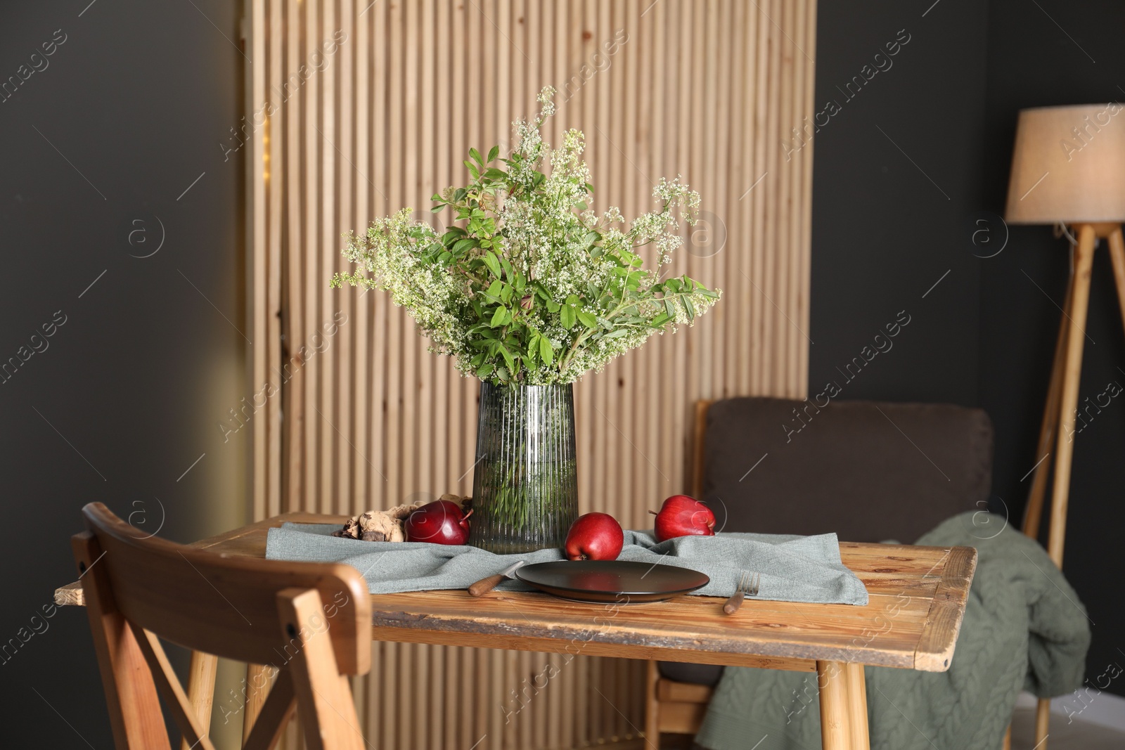 Photo of Set of clean dishware, ripe red apples and flowers on wooden table in stylish dining room