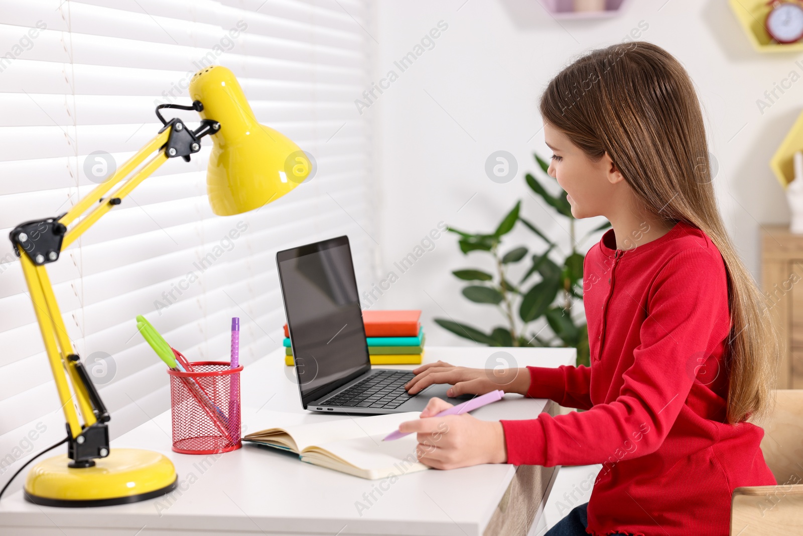 Photo of E-learning. Cute girl taking notes during online lesson at table indoors