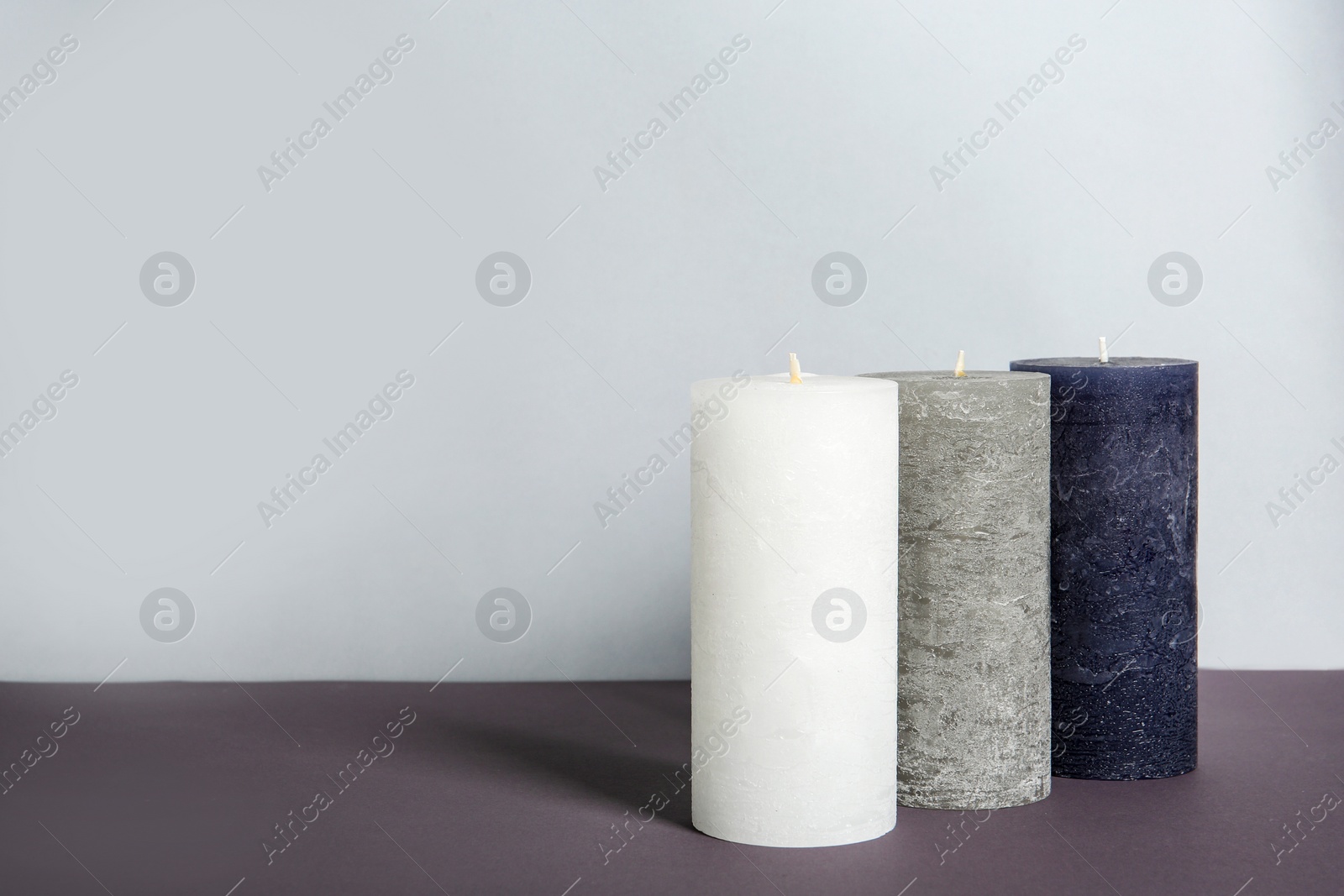 Photo of Decorative wax candles on table against light background