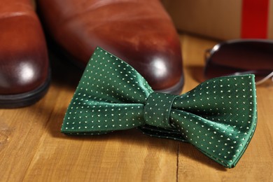 Stylish green bow tie and brown shoes on wooden background, closeup