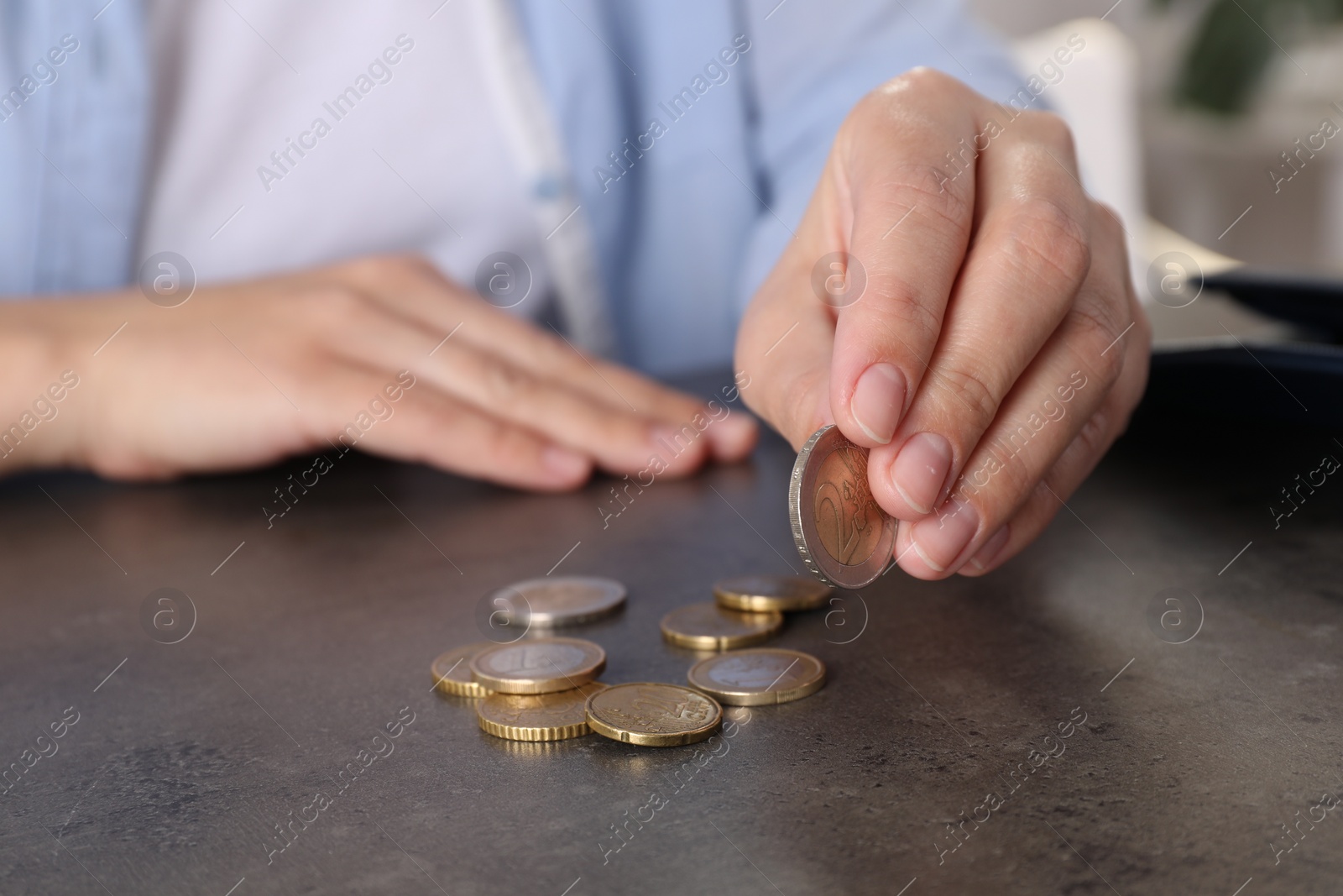 Photo of Poor woman counting coins at grey table indoors, closeup