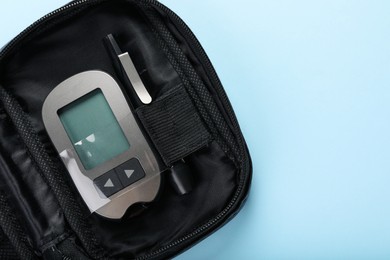 Digital glucometer and lancet pen in bag on light blue background, top view with space for text. Diabetes control