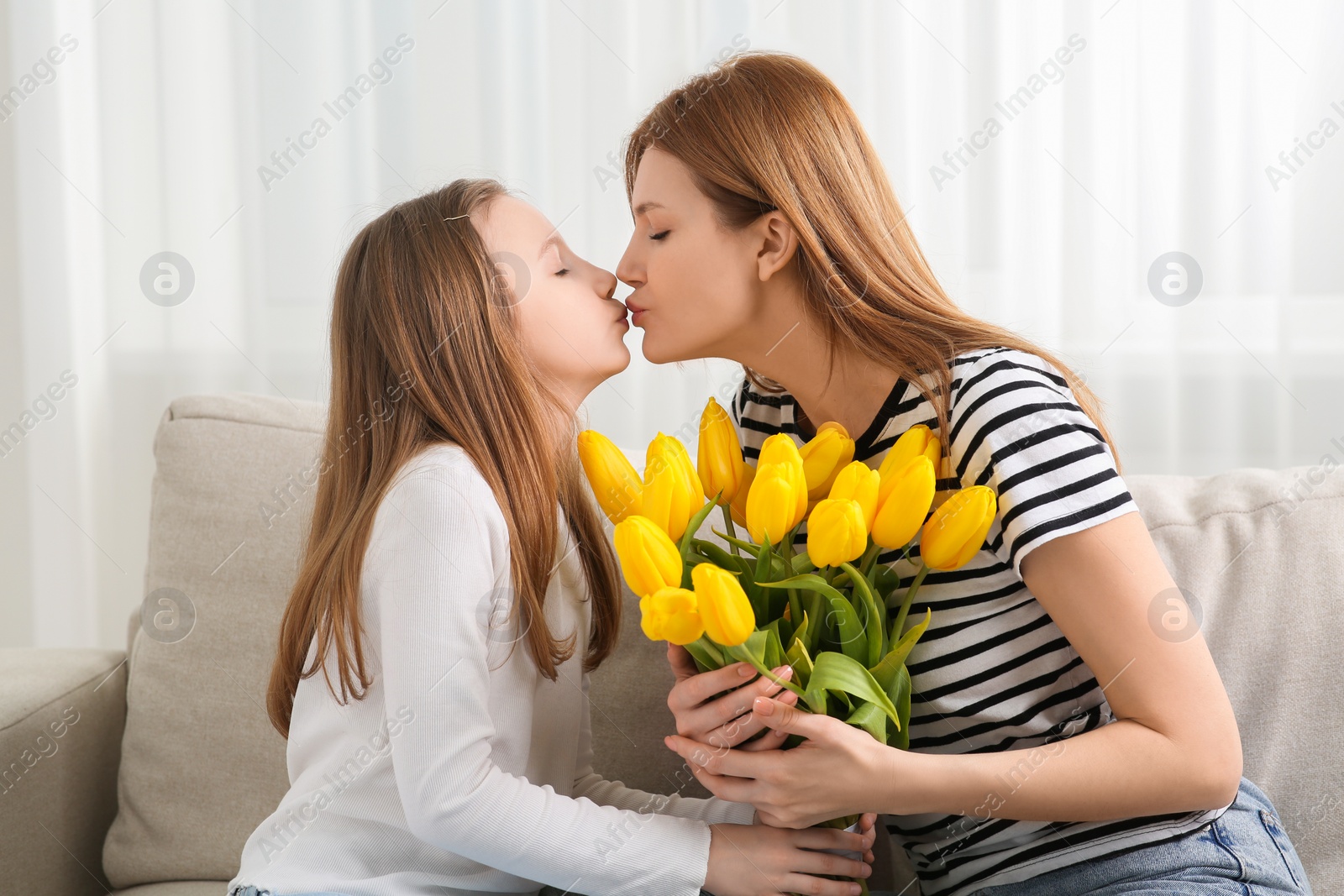 Photo of Mother and her cute daughter with bouquet of yellow tulips on sofa at home