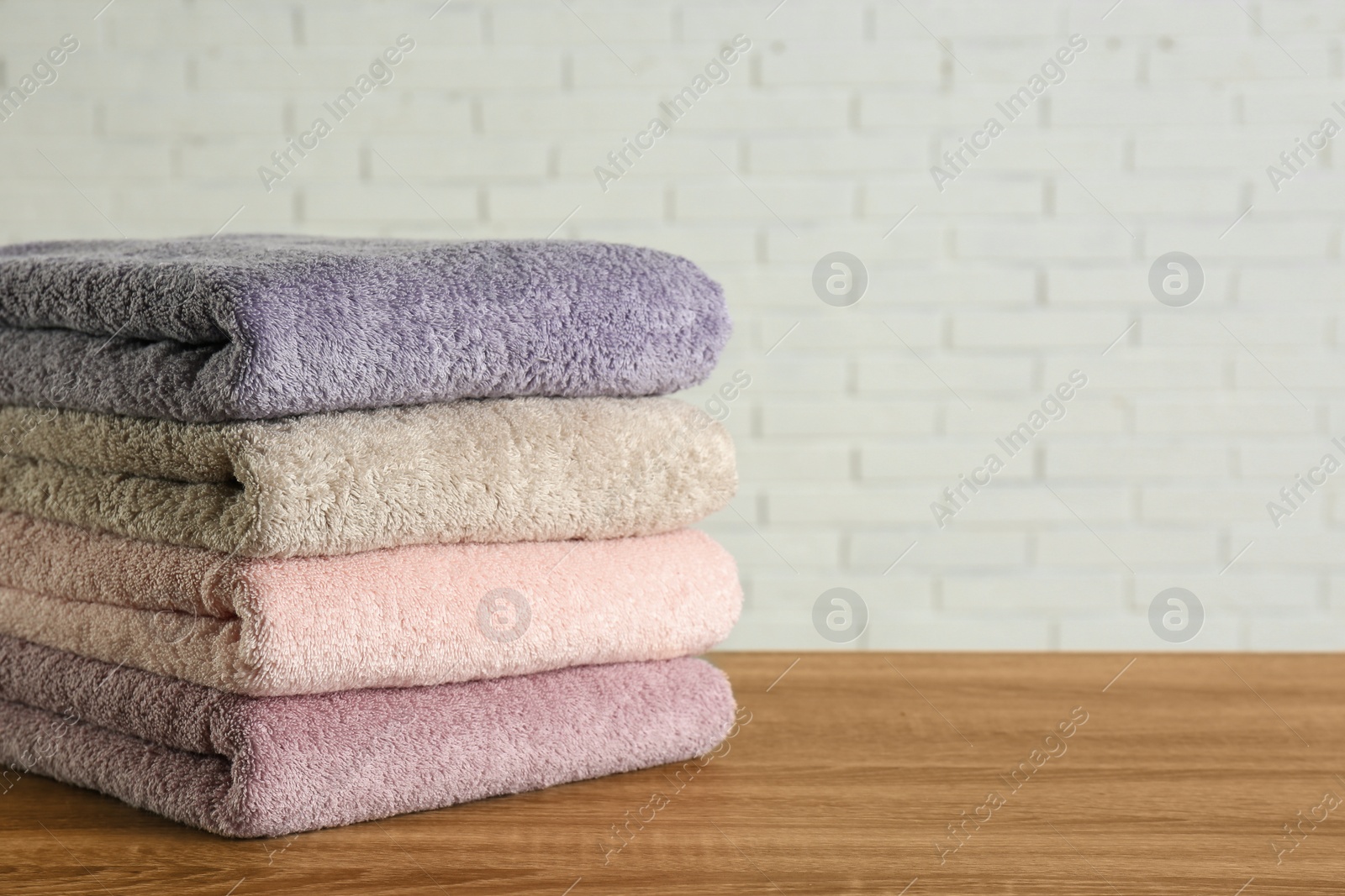 Photo of Stack of clean bath towels on wooden table near white brick wall. Space for text
