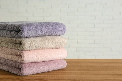 Photo of Stack of clean bath towels on wooden table near white brick wall. Space for text