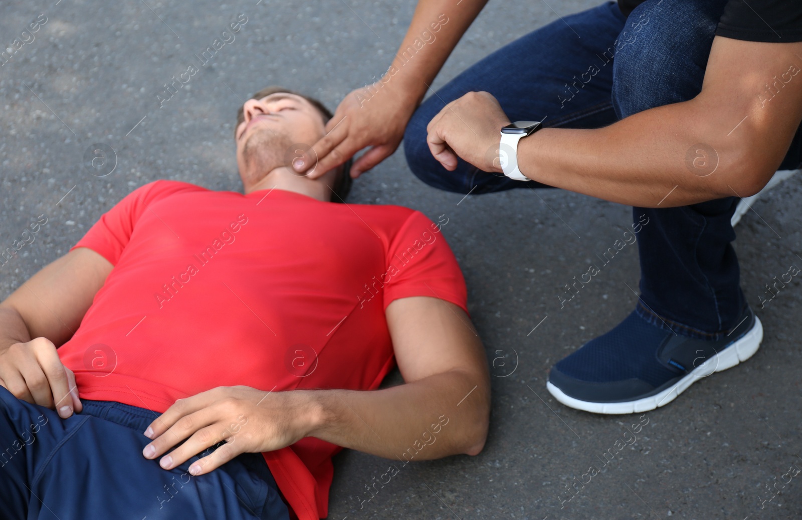 Photo of Passerby checking pulse of unconscious young man outdoors