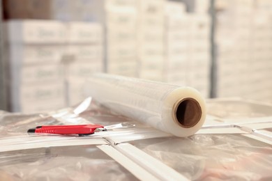 Roll of stretch film and utility knife on wrapped boxes in warehouse