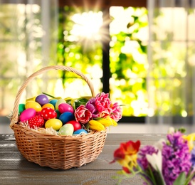 Image of Colorful Easter eggs in wicker basket on wooden table indoors