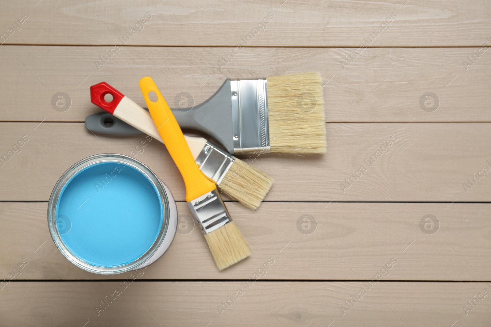 Photo of Can of light blue paint and brushes on wooden table, flat lay. Space for text