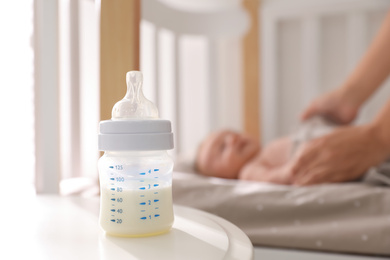 Photo of Mother and little baby indoors, focus on table with bottle of milk