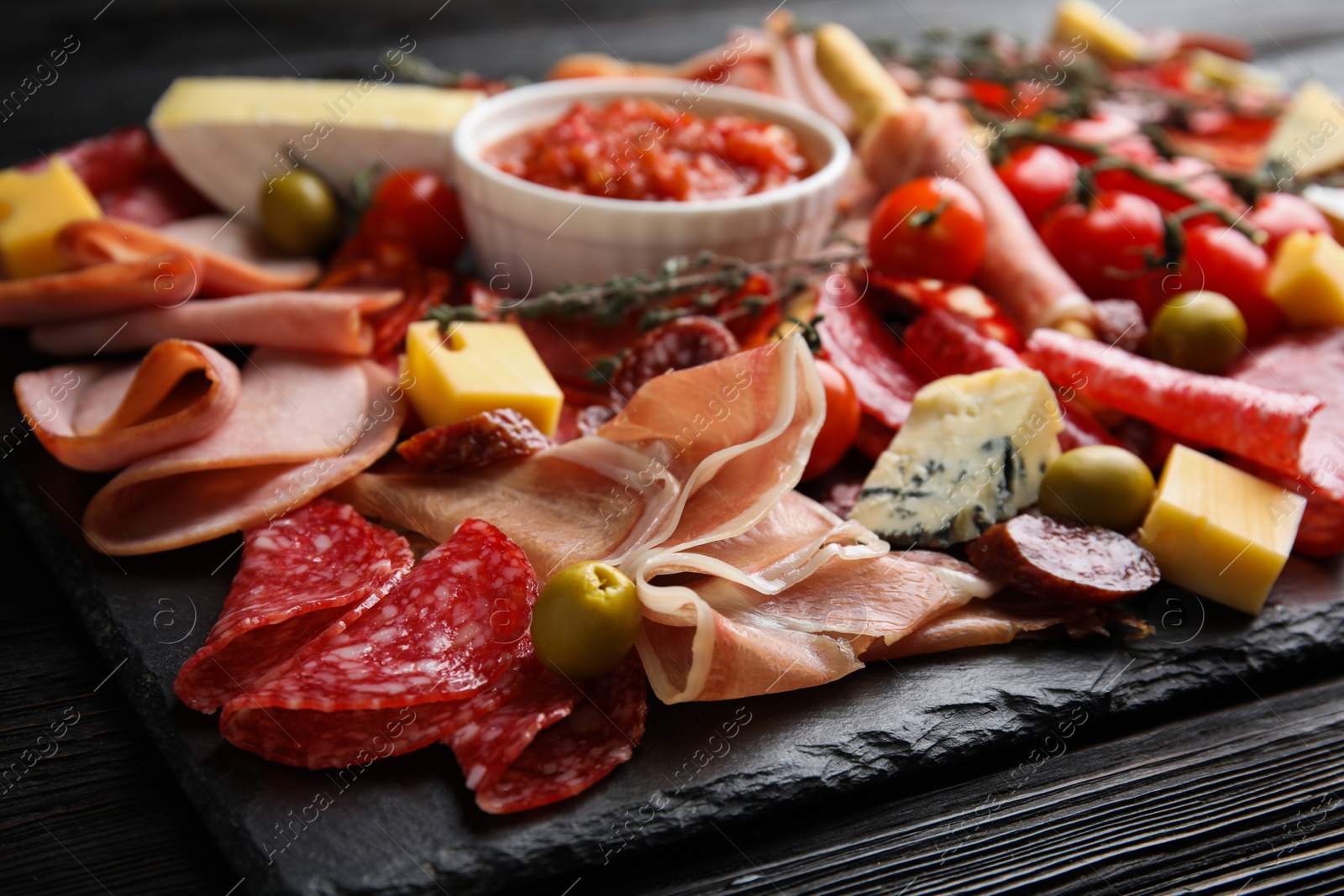 Photo of Tasty ham with other delicacies served on black wooden table, closeup