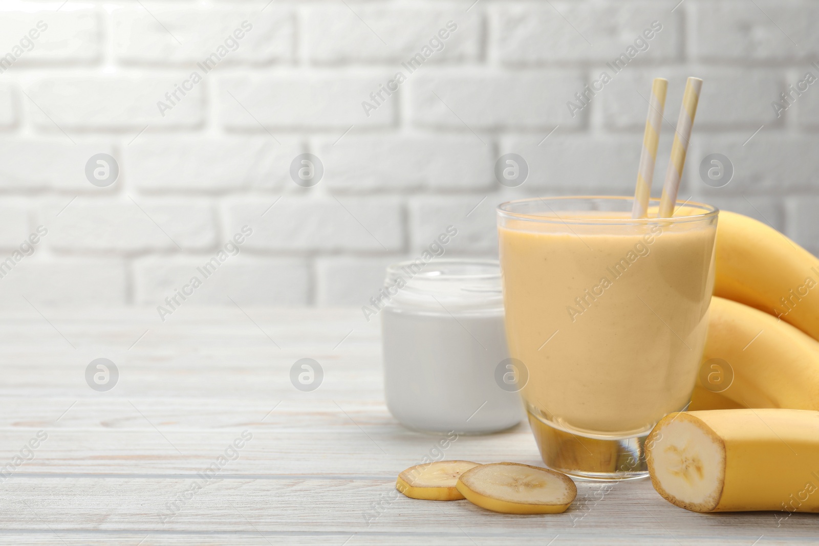 Photo of Glass of tasty banana smoothie with straws and ingredients on white wooden table. Space for text