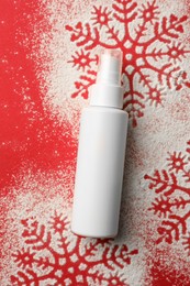 Photo of Winter skin care. Hand cream and snowflake silhouettes made with artificial snow on red background, top view