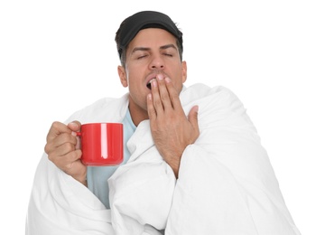 Man in sleeping mask wrapped with blanket holding cup on white background