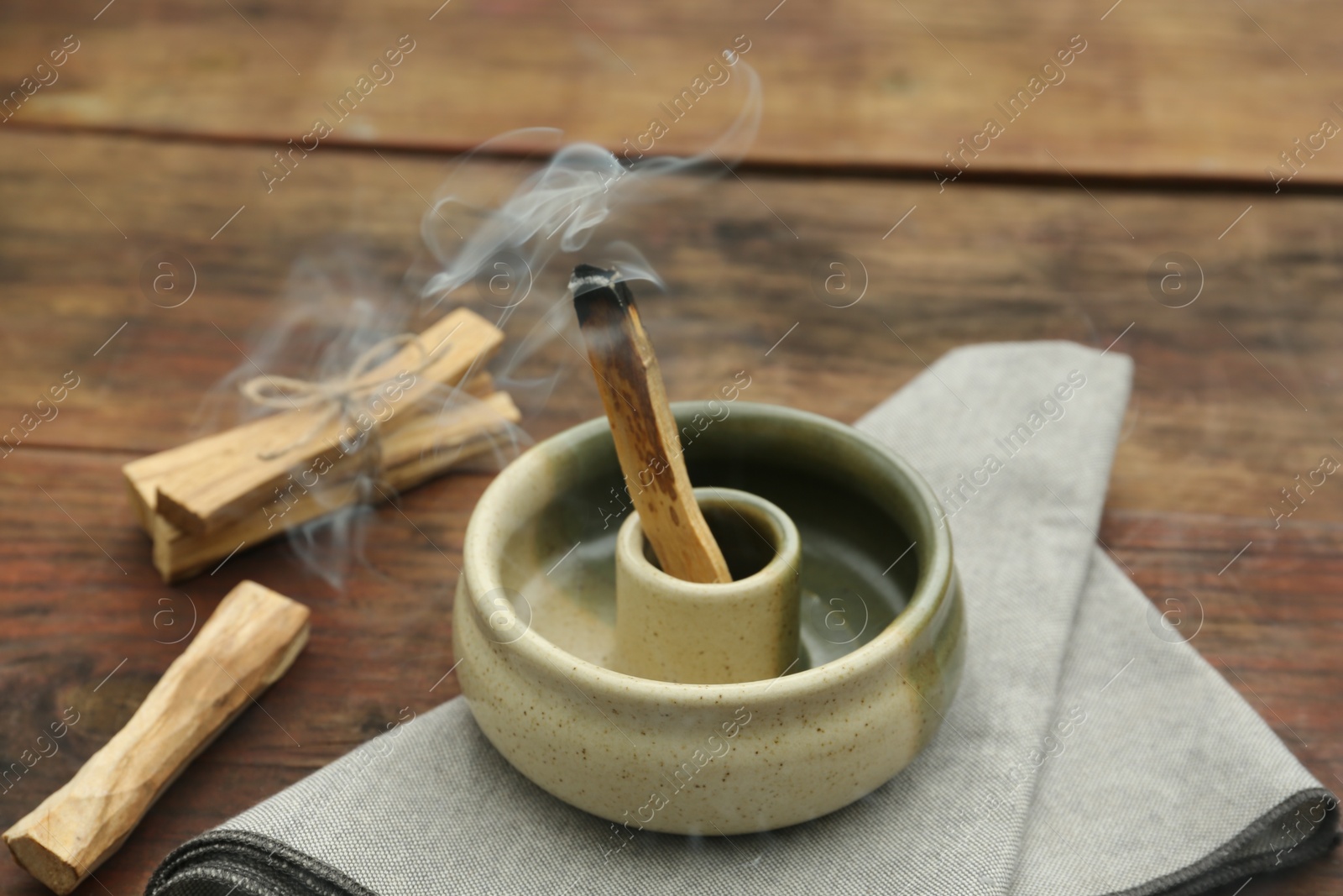 Photo of Palo Santo stick smoldering in holder on wooden table