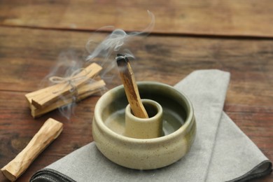 Palo Santo stick smoldering in holder on wooden table