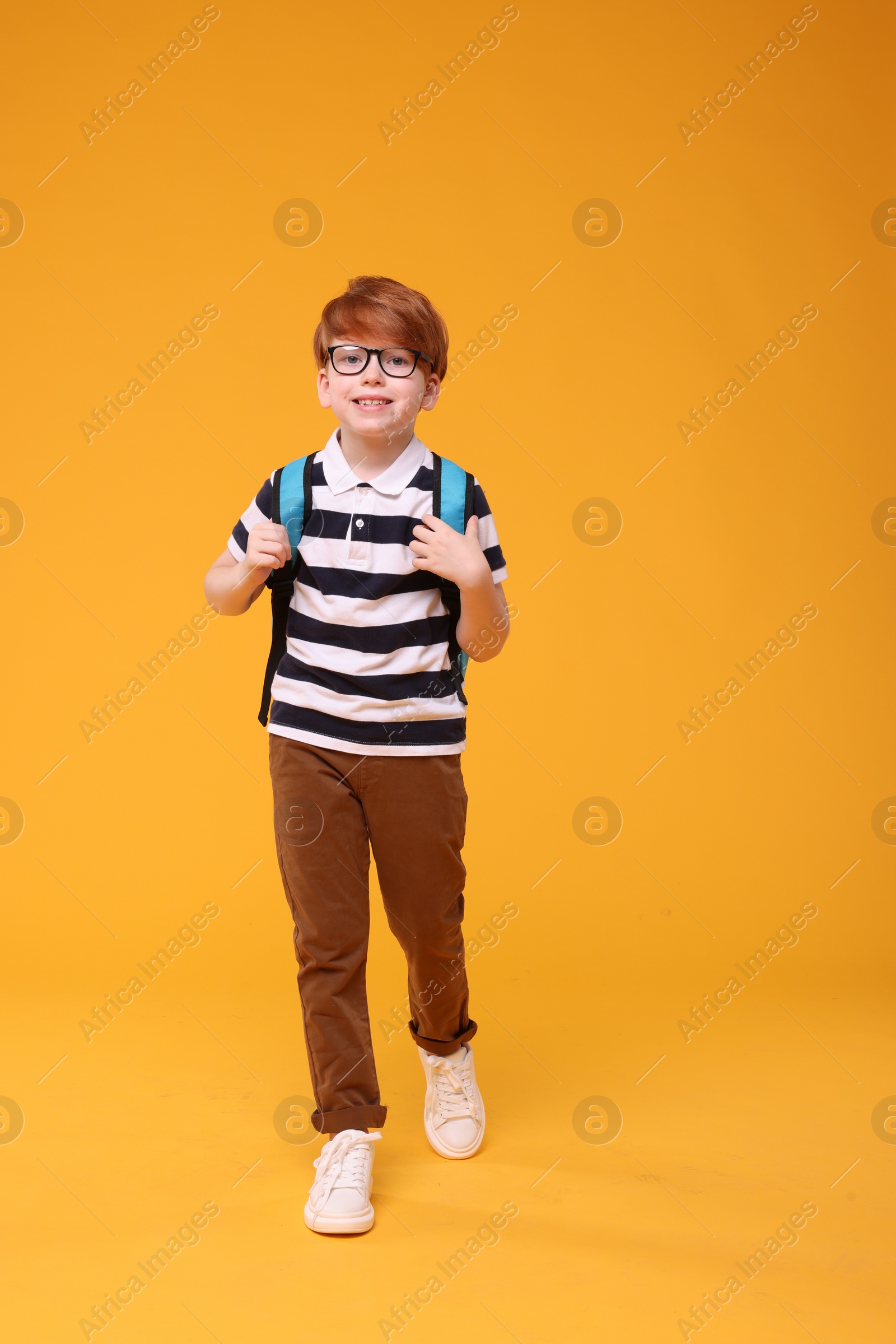 Photo of Happy schoolboy in glasses on orange background