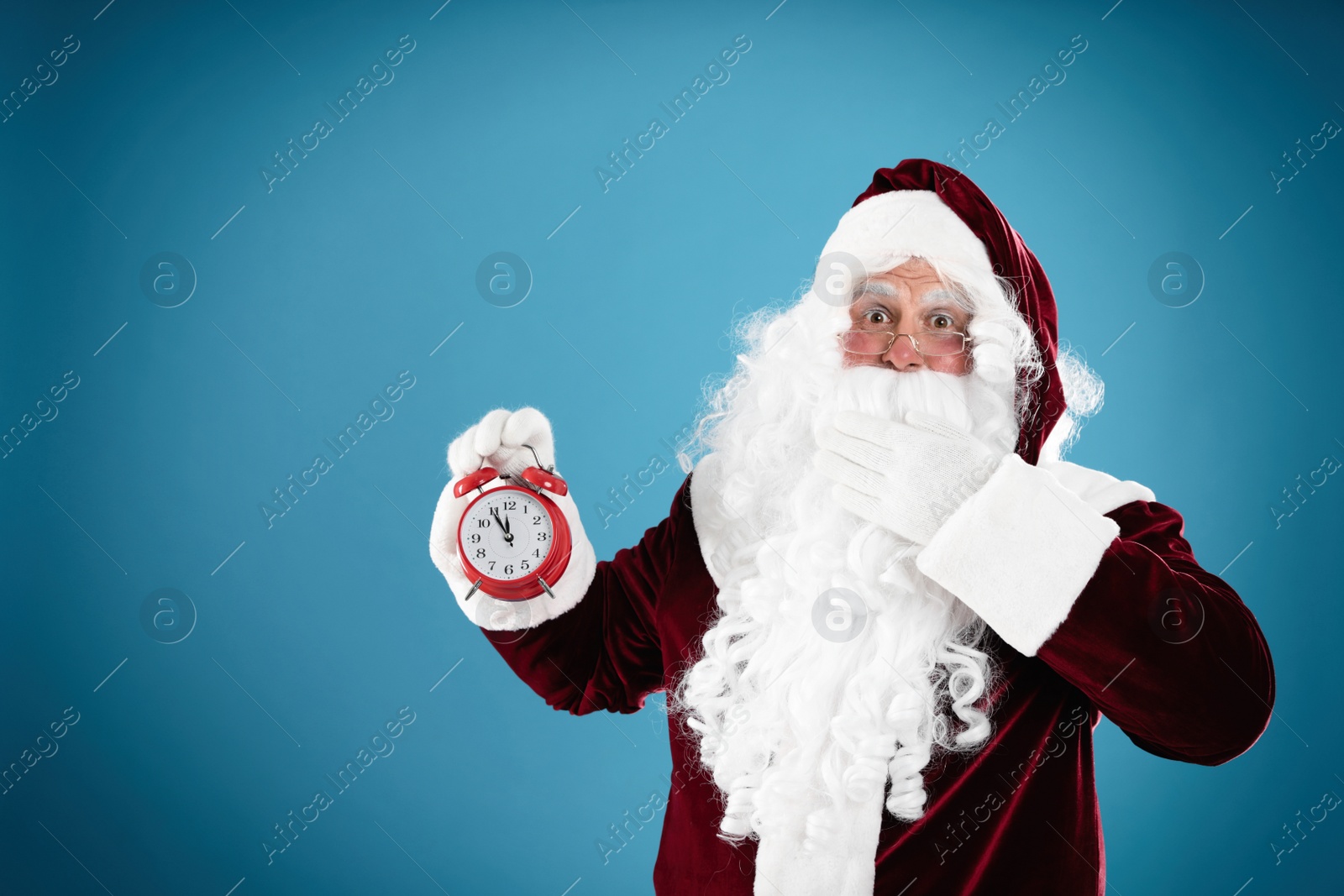 Photo of Santa Claus holding alarm clock on blue background, space for text. Christmas countdown