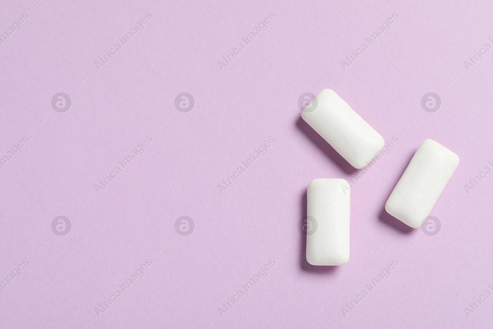 Photo of Tasty white chewing gums on lilac background, flat lay. Space for text