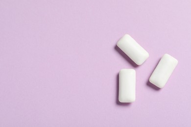 Photo of Tasty white chewing gums on lilac background, flat lay. Space for text