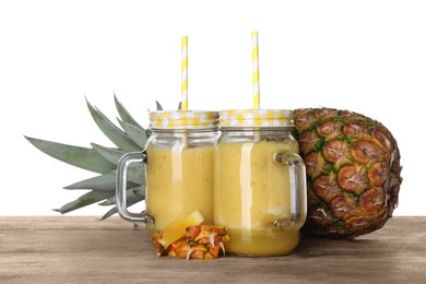 Photo of Tasty pineapple smoothie in mason jars and fruit on wooden table against white background