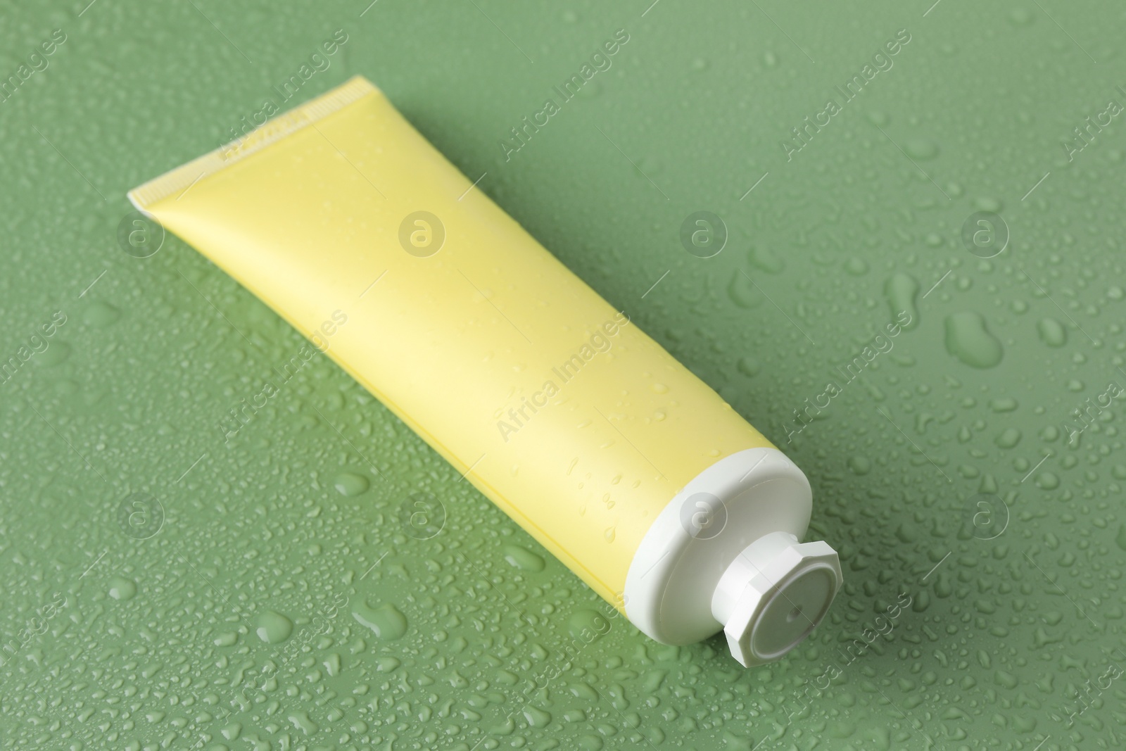 Photo of Moisturizing cream in tube on green background with water drops, closeup