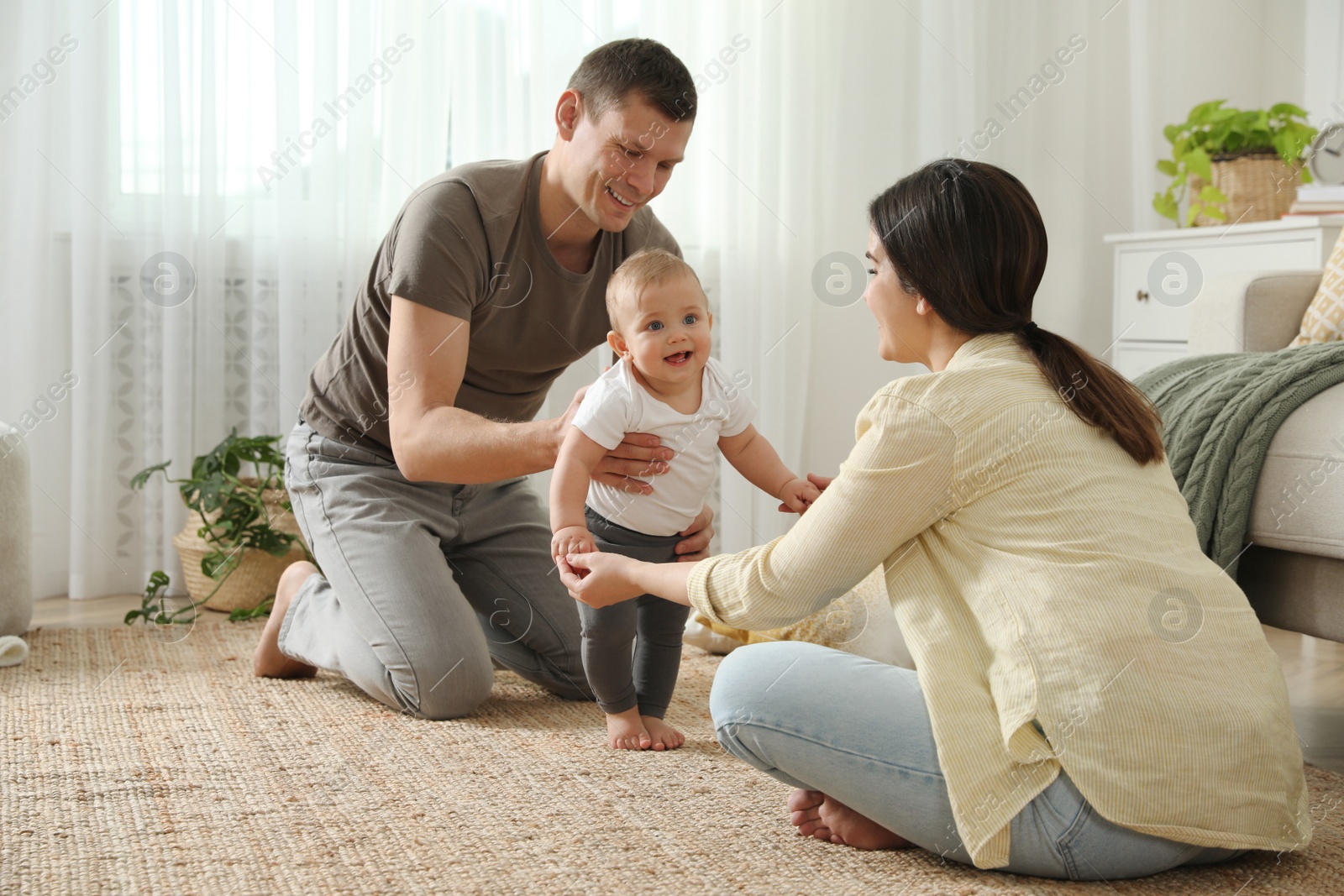 Photo of Parents supporting their baby daughter while she learning to walk at home