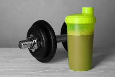 Photo of Bottle with protein shake and dumbbell on wooden table