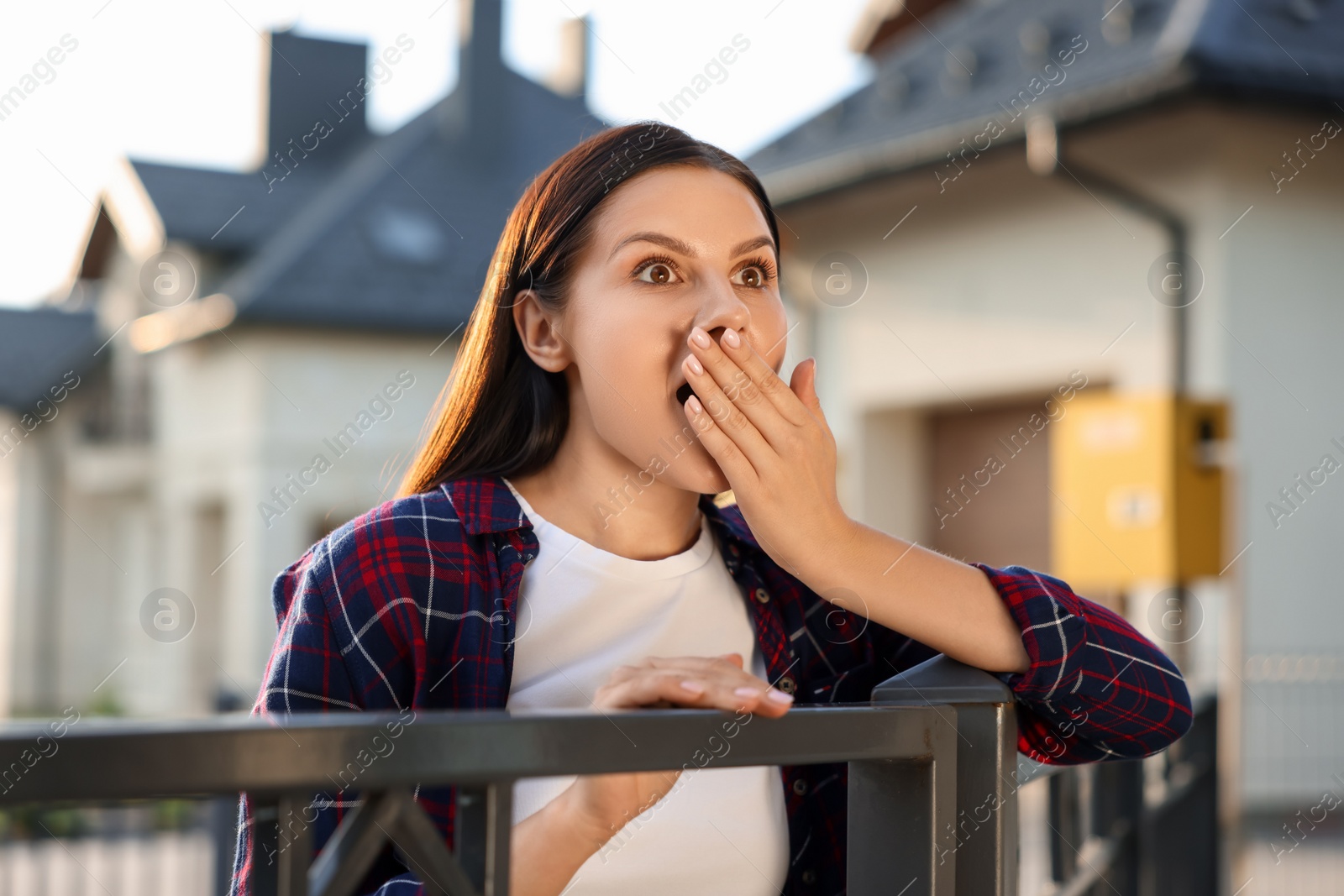 Photo of Concept of private life. Curious young woman spying on neighbours over fence outdoors