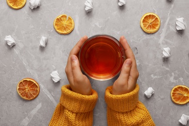 Photo of Woman holding cup of hot tea at grey marble table, top view. Cozy winter