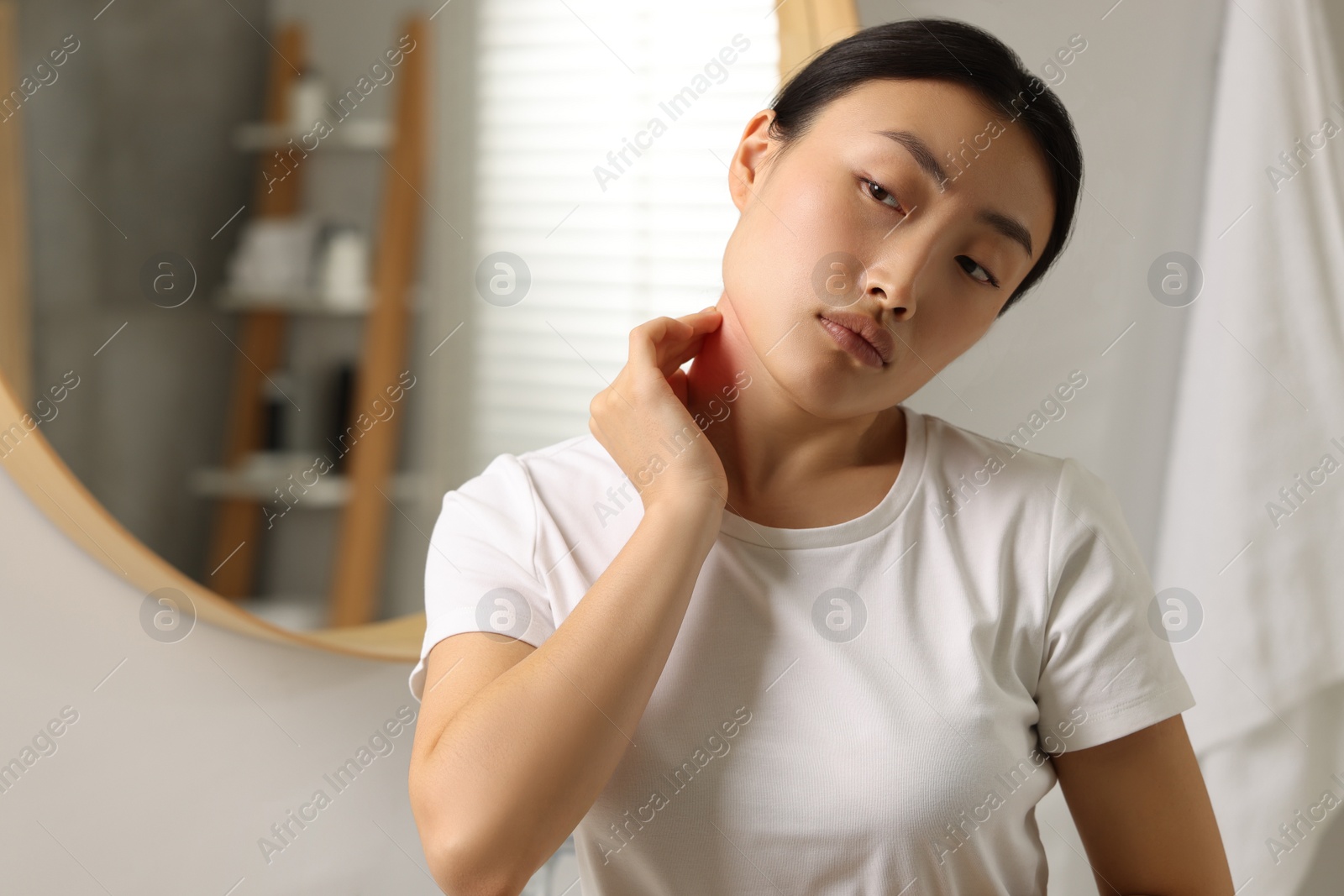 Photo of Suffering from allergy. Young woman scratching her neck near mirror in bathroom, space for text