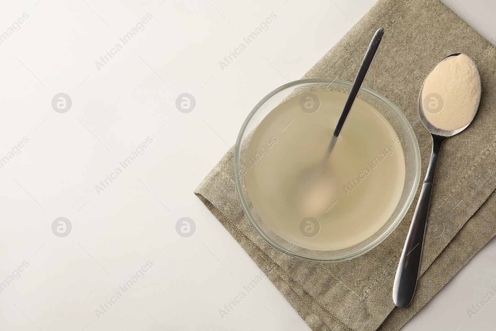 Photo of Glass bowl of agar-agar jelly and spoon with powder on white marble table, top view. Space for text