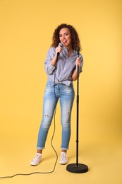 Curly African-American woman singing in microphone on color background