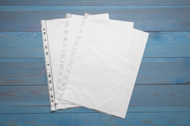 Photo of Punched pockets with paper sheets on light blue wooden table, flat lay. Space for text