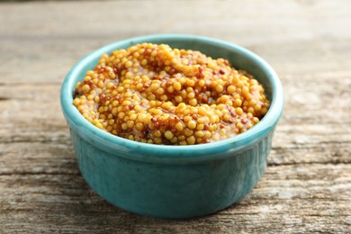 Fresh whole grain mustard in bowl on wooden table, closeup