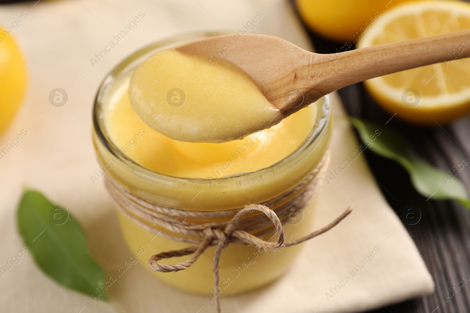 Photo of Taking delicious lemon curd from glass jar at table, closeup