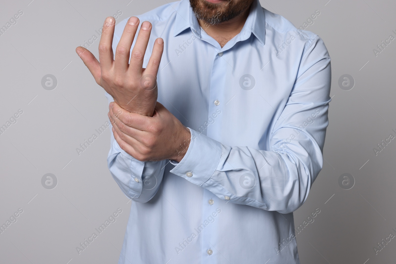 Photo of Man suffering from pain in his hand on light background, closeup. Arthritis symptoms