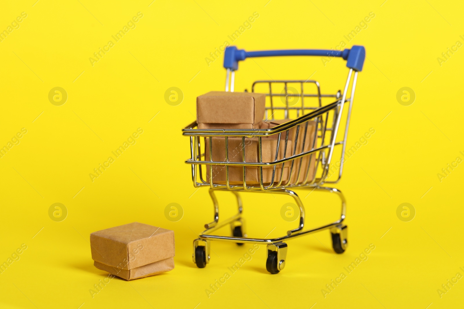 Photo of Small metal shopping cart with boxes on yellow background